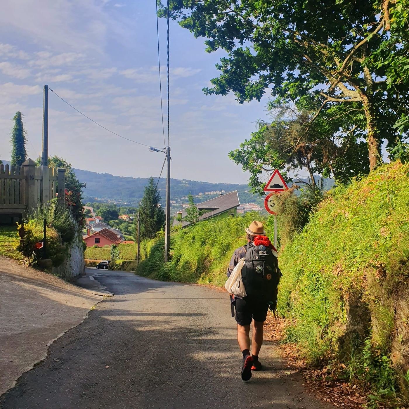 Un pellegrino con cappello di paglia e zaino cammina lungo una strada di campagna della Galizia