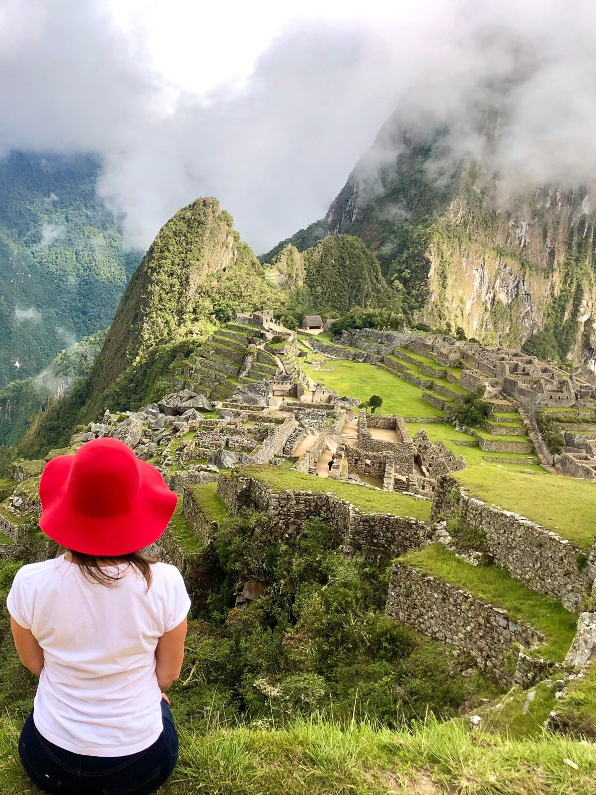 Gea, Epic Router del Capitolo di Milano di Epic Routes Community, di spalle con un cappello rosso mentre guarda Machu Picchu e il Huayna Picchu avvolti dalle nuvole, in Perù