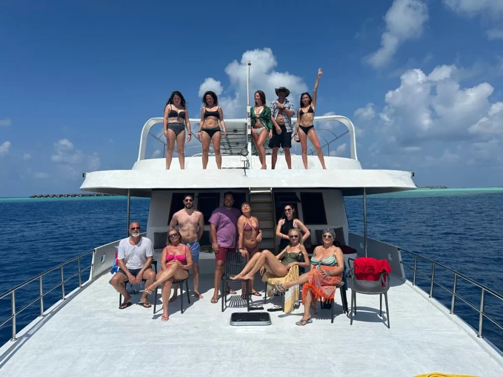 Gruppo di viaggiatori di Epic Routes Community sul ponte di una barca in navigazione tra gli atolli delle Maldive, con mare blu e laguna turchese sullo sfondo