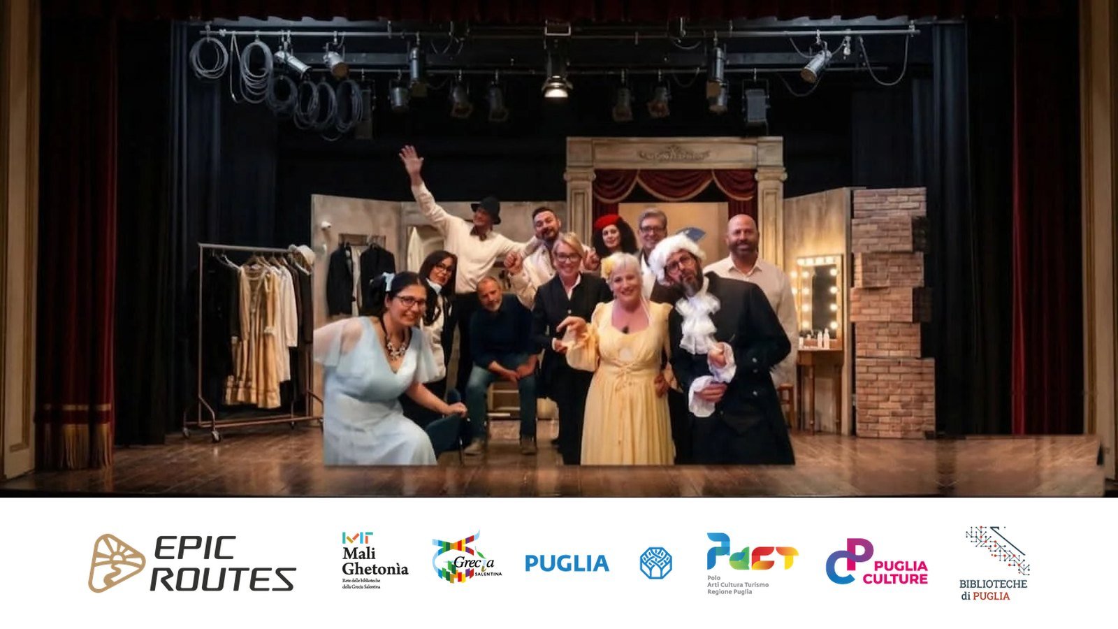 Il cast del Gruppo Teatroadunpasso in costume sul palco, con il logo di Epic Routes Community e i loghi di Mali Ghetonìa e dei partner istituzionali