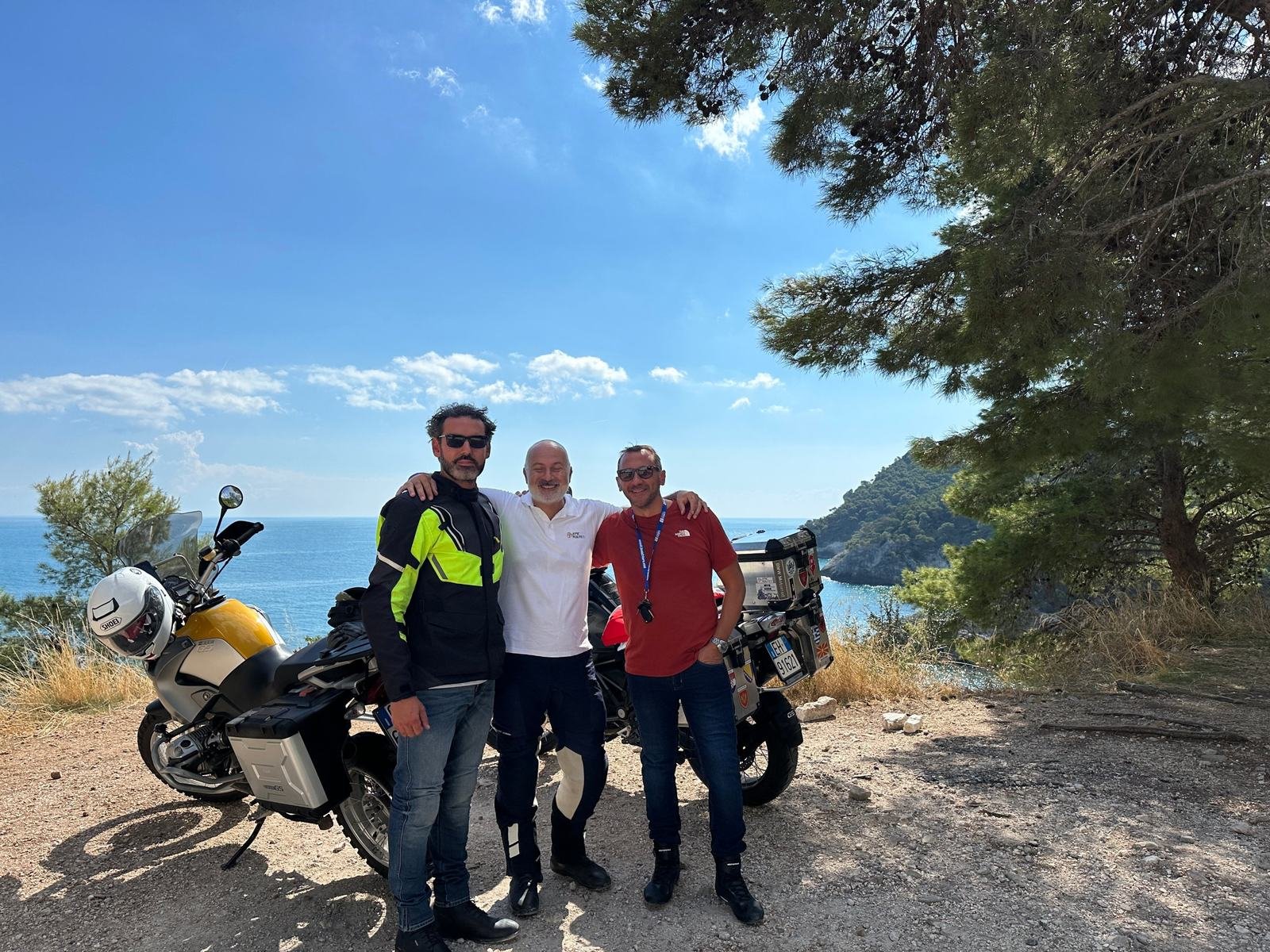 Tre motociclisti di Epic Routes Community accanto alle loro moto da viaggio, con il mare del Gargano alle spalle