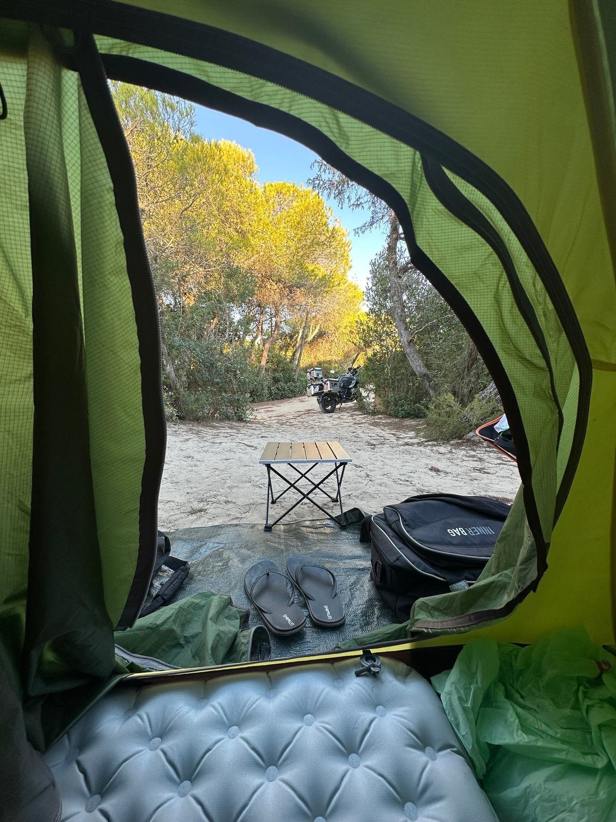La moto da viaggio vista dall'ingresso della tenda, nella pineta di Marina di Ugento, durante un raduno di motoviaggiatori