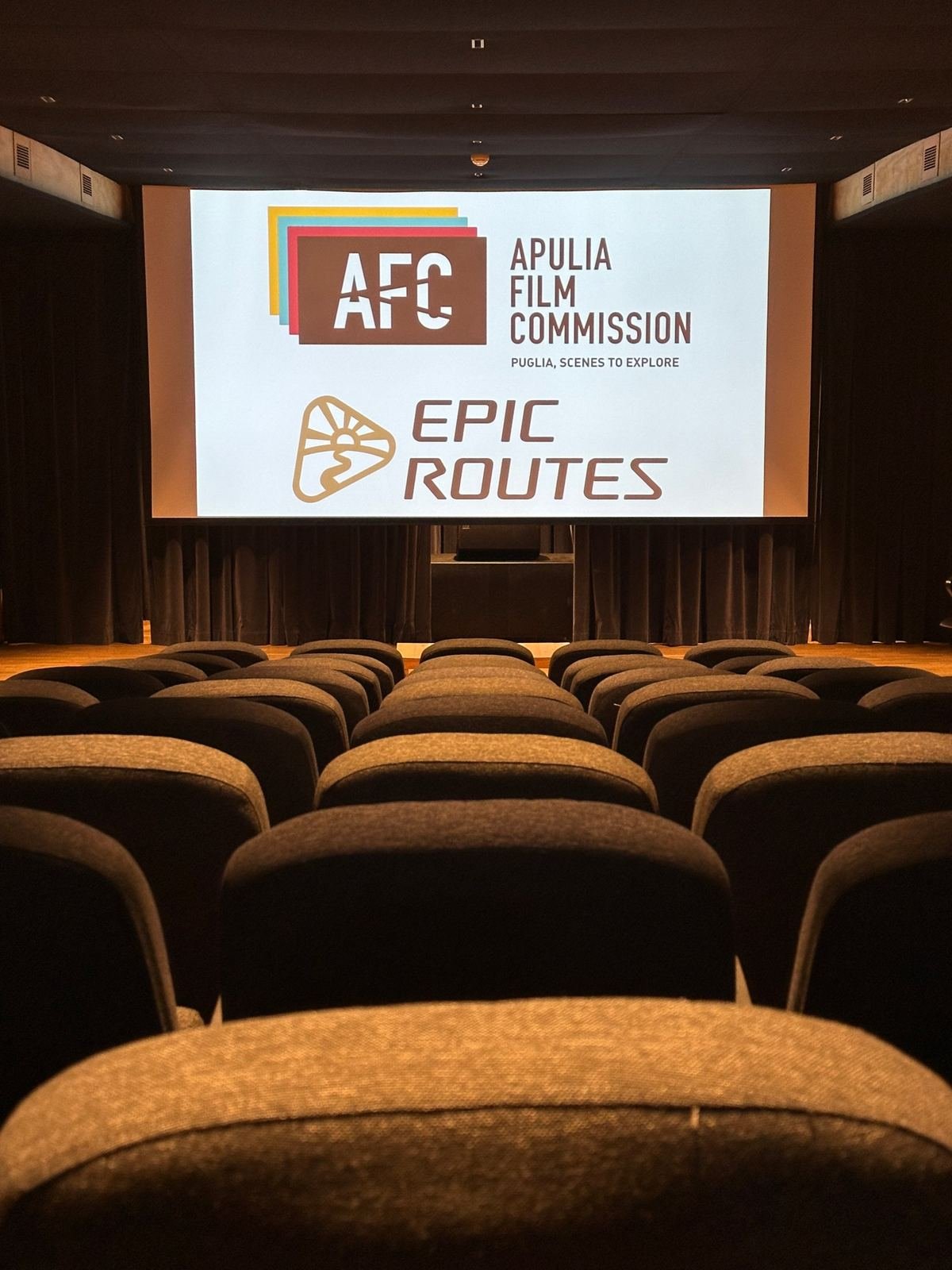 I loghi di Apulia Film Commission ed Epic Routes sul grande schermo del Cineporto di Lecce, prima della proiezione