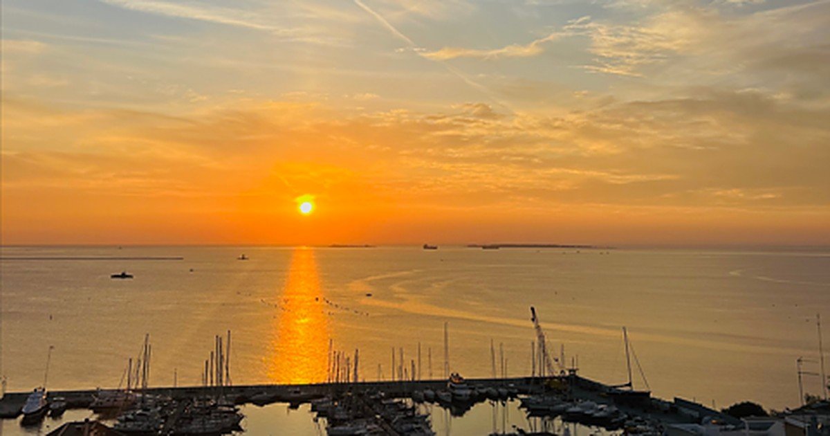 Tramonto sul Mar Grande di Taranto, con il sole che si riflette sul mare e le barche ormeggiate nel porto