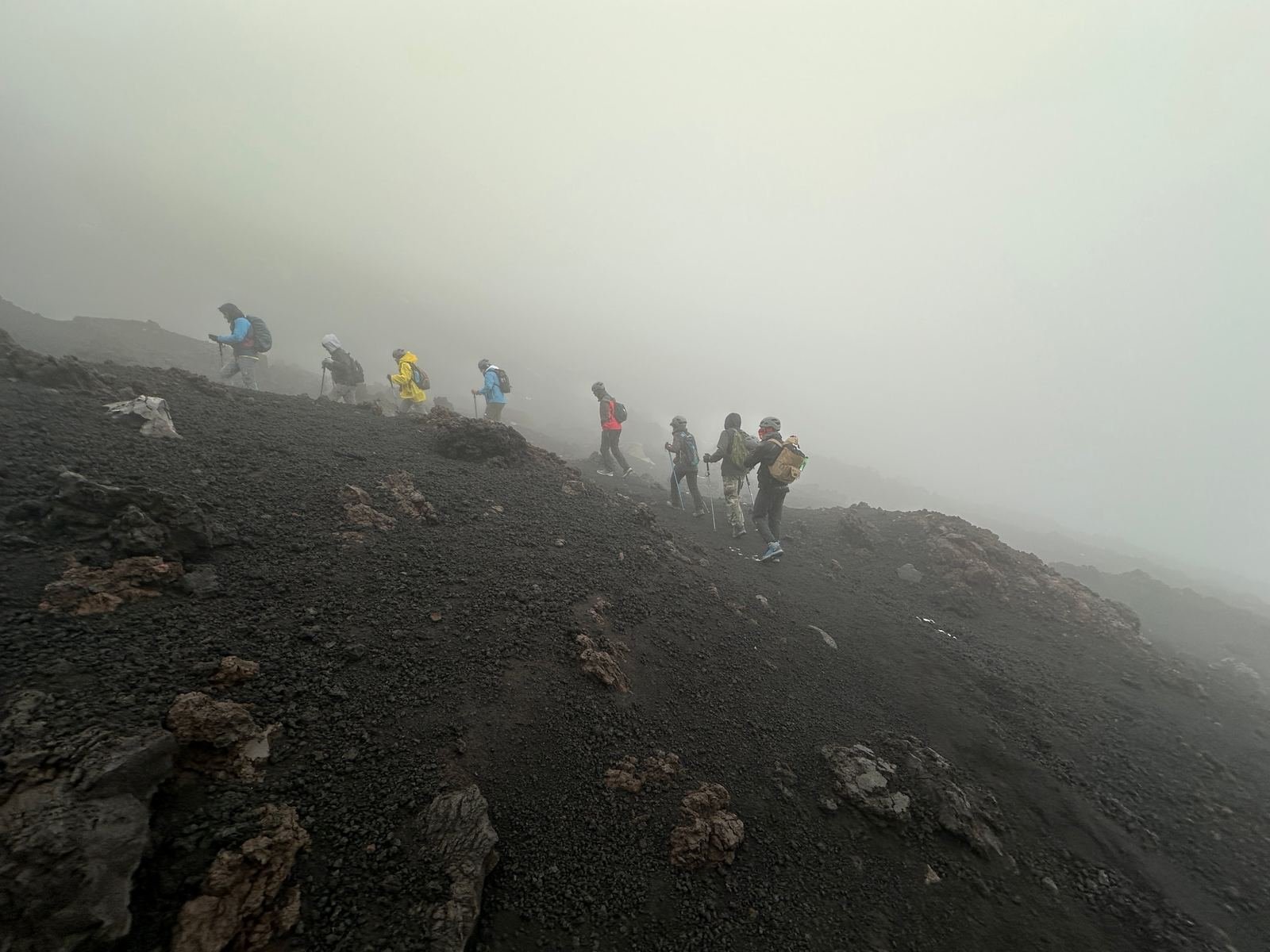 Escursionisti di Epic Routes Community in fila nella nebbia sul pendio di lava nera dell'Etna