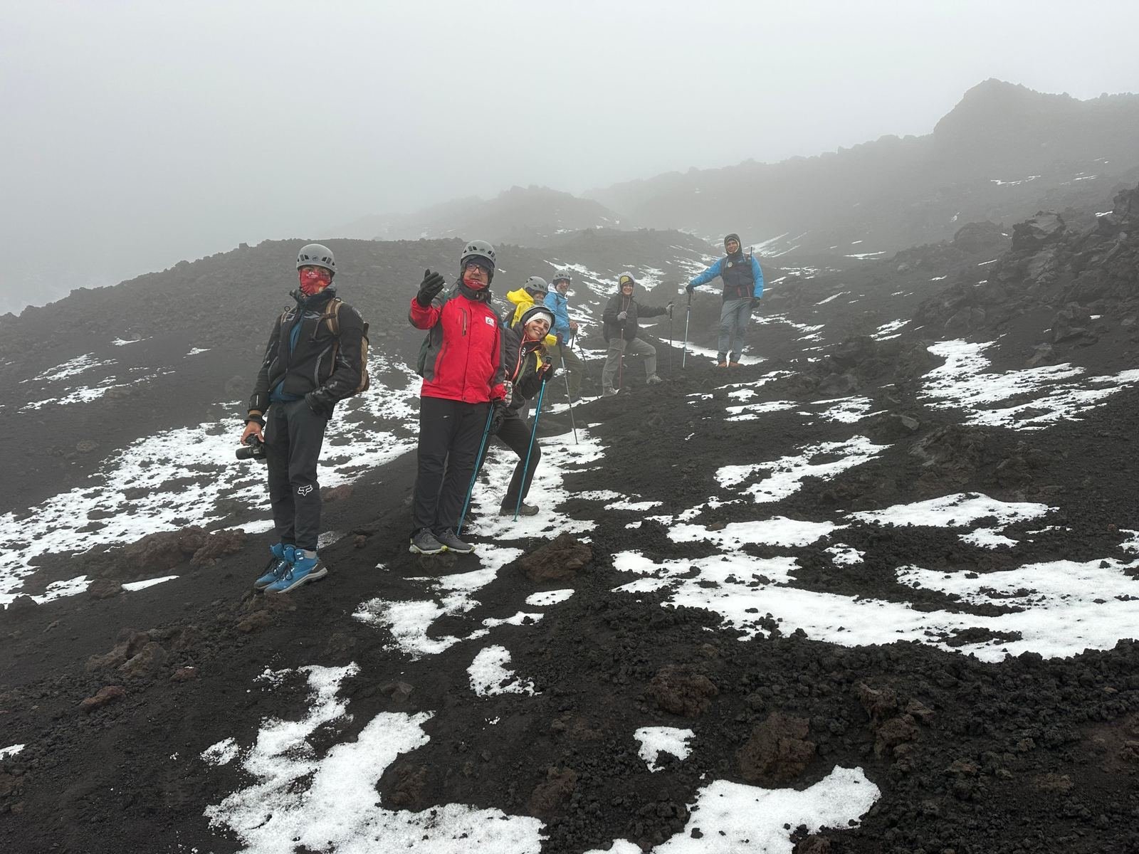 Escursionisti di Epic Routes Community con casco e bastoncini tra neve e lava nera, verso i crateri sommitali dell'Etna