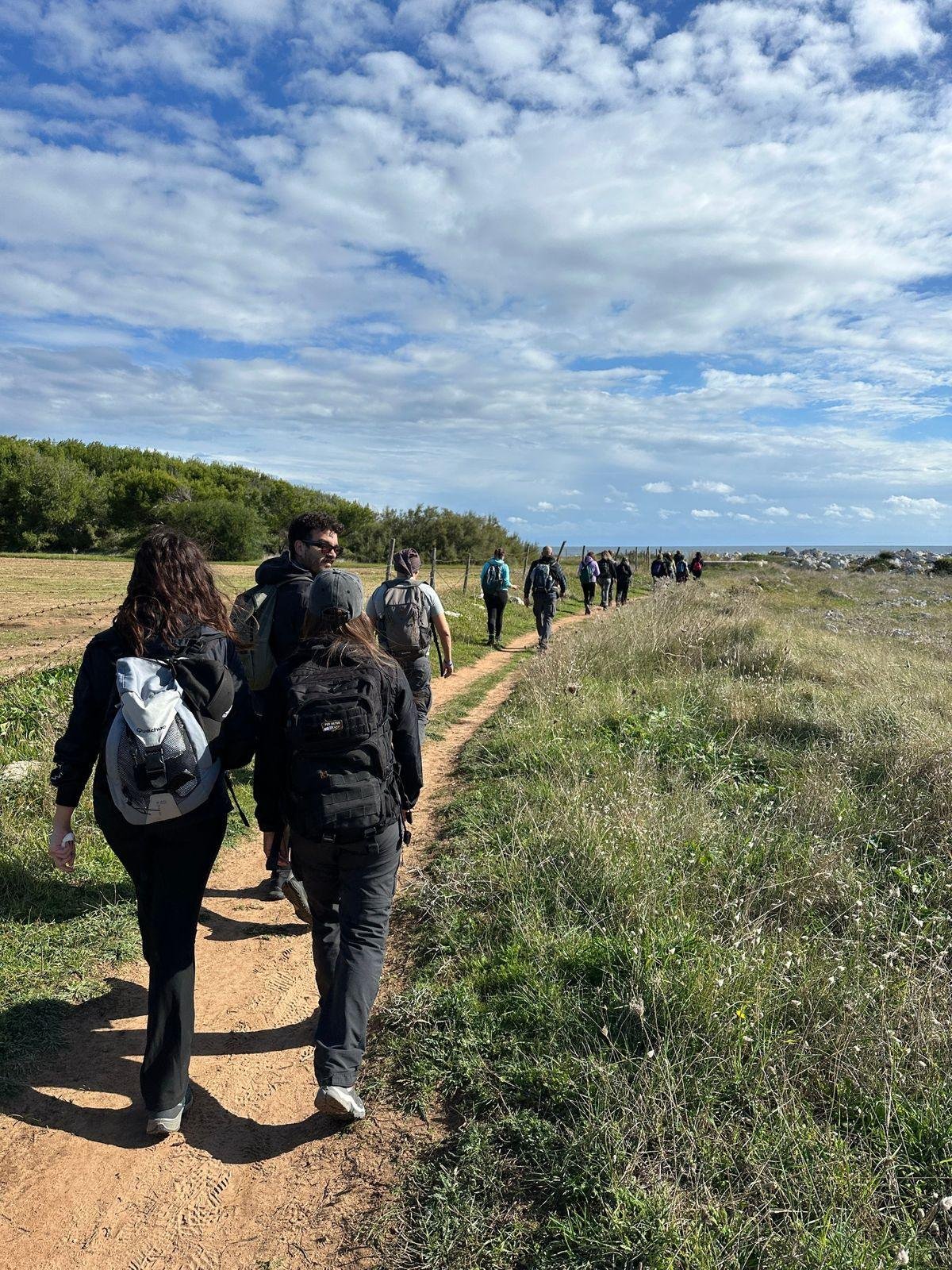 Escursionisti di Epic Routes Community in fila su un sentiero di terra rossa che porta verso il mare del Salento
